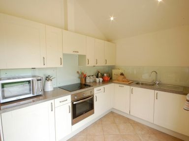A kitchen with white cabinets a microwave oven a stove a kettle a teapot a bread bin and a sink at Remus Larling near East Harling