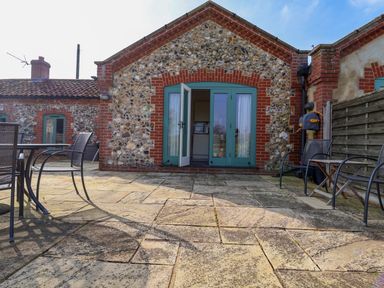A stone patio with metal chairs and a table outside a stone and brick building with green patio doors at Remus Larling near East Harling