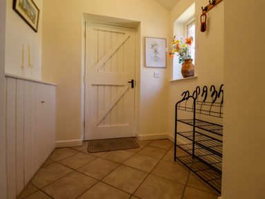 A hallway with a wooden door a tile floor a shoe rack and a window with a vase of flowers at Remus in Larling near East Harling
