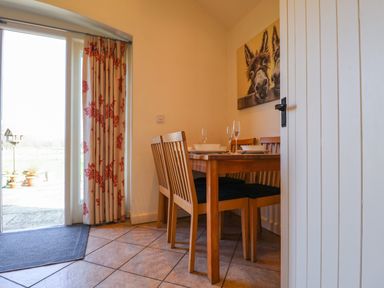 A dining area with a wooden table set with plates and glasses and wooden chairs near a glass door with floral curtains at Remus Larling near East Harling