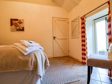 A bedroom with a bed covered with folded towels a door a mirror on the wall patterned curtains and a chair near a glass door at Remus Larling near East Harling