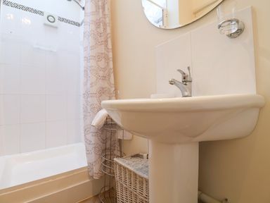A bathroom with a pedestal sink shower with curtain and wicker storage basket at Remus Larling near East Harling