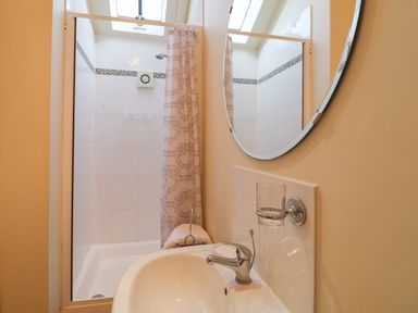 A bathroom with a sink faucet a round mirror and a shower area with a curtain at Remus Larling near East Harling