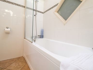 A bathroom with a white bathtub tiled walls and a window at Remus Larling near East Harling