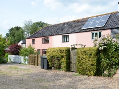 A pink house with solar panels on the roof a wooden gate and hedges in front at Seafarers in Fressingfield