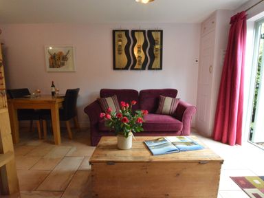 A living room with a purple sofa wooden coffee table with flowers and an open book and a dining table with chairs at Seafarers in Fressingfield