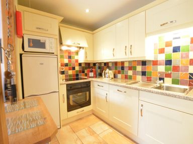 A kitchen with white cabinets colorful tiled backsplash oven microwave fridge and double sink at Seafarers in Fressingfield