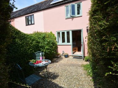 A small courtyard with a metal table and chairs and an open door to a pink house at Seafarers in Fressingfield