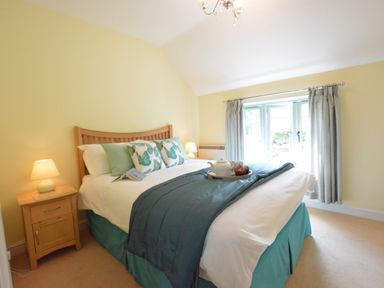 A bedroom with a wooden bed frame bedside tables lamps and a window with curtains at Seafarers in Fressingfield