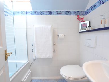 A bathroom with a towel rail holding a white towel a toilet a sink and a shower with glass doors at Seafarers in Fressingfield