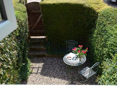 A small outdoor seating area with a metal table and two chairs surrounded by trimmed hedges at Seafarers in Fressingfield
