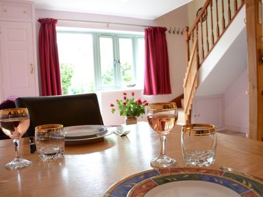 A dining table set with plates and glasses near a window with red curtains and a wooden staircase in a dining room at Seafarers in Fressingfield