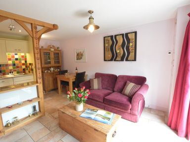 A living room with a burgundy sofa a wooden chest coffee table and a dining area at Seafarers in Fressingfield