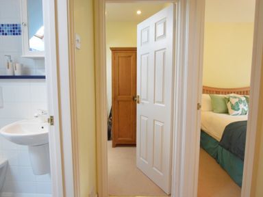 A hallway with doors leading to a bathroom with a sink and a bedroom with a bed and a wardrobe at Seafarers in Fressingfield
