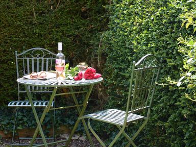 A small metal table with two chairs in a garden with a bottle of wine two glasses a bouquet of red roses and a pair of sunglasses at Seafarers in Fressingfield