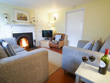 A living room with a fireplace two grey sofas a small table with wine and glasses and a leather chair at Aldeburgh Cottage in Aldeburgh