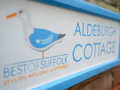 A sign with a blue and white bird and text Aldeburgh Cottage at Aldeburgh