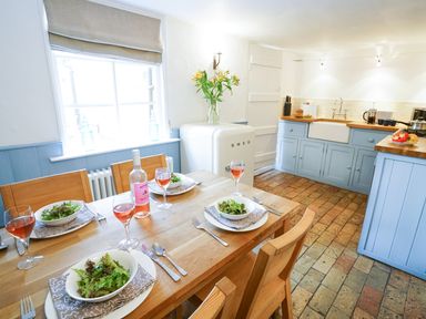 A kitchen with a wooden dining table set for four with wine and salad bowls next to blue cabinets and a white smeg fridge at Aldeburgh Cottage in Aldeburgh