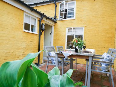 An outdoor patio with a table and four chairs next to yellow painted brick walls at Aldeburgh Cottage in Aldeburgh