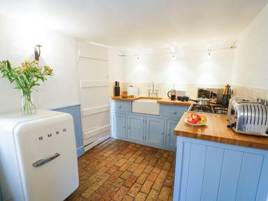 A kitchen with blue cabinets wood countertops a white Smeg fridge and tiled floor at Aldeburgh Cottage in Aldeburgh
