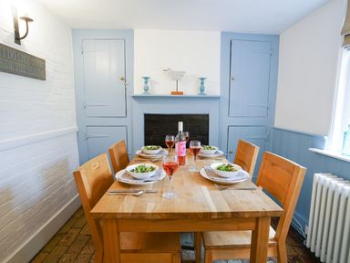 A dining room with a wooden table set with plates bowls and wine glasses surrounded by wooden chairs at Aldeburgh Cottage in Aldeburgh