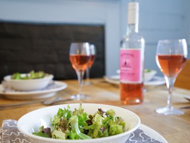 A dining table set with bowls of green salad and glasses of rose wine at Aldeburgh Cottage in Aldeburgh
