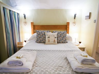 A bedroom with a wooden bed frame pillows folded towels bedside tables and lamps at Aldeburgh Cottage in Aldeburgh