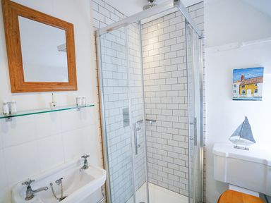 A bathroom with a shower enclosure with white tiled walls a sink with a mirror above and a toilet with a wooden seat at Aldeburgh Cottage in Aldeburgh