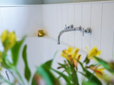 A bathtub with wall mounted silver faucet and yellow flowers in the foreground at Aldeburgh Cottage in Aldeburgh