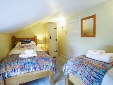 A bedroom with two single beds covered with colorful blankets and white towels a wooden wardrobe a mirror on the wall and a small bedside table with a lamp at Aldeburgh Cottage in Aldeburgh
