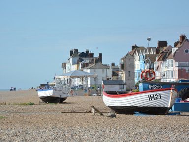A pebble beach with boats and buildings in the background at Mariners Cottage in Aldeburgh