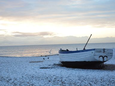 A small boat named Viking on a snowy beach with the sea and cloudy sky in the background