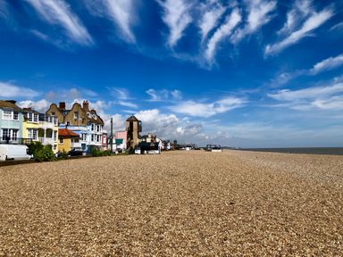 A pebble beach with colorful houses lined up along the shore and a partly cloudy sky at Mariners Cottage in Aldeburgh