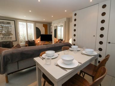 A dining table set with bowls and glasses in a living room with a sofa chairs and a television at Mariners Cottage in Aldeburgh