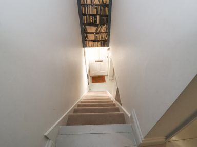 A staircase with carpeted steps leading to a white door with a doormat at Mariners Cottage in Aldeburgh
