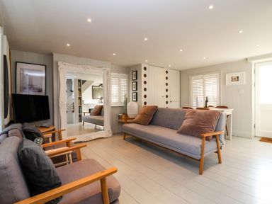 A living room with grey sofas a large decorative mirror a small dining table and white shutters at Mariners Cottage in Aldeburgh