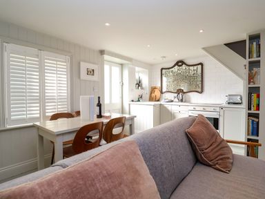 A kitchen and dining area with a table and chairs and a sofa with pillows at Mariners Cottage in Aldeburgh