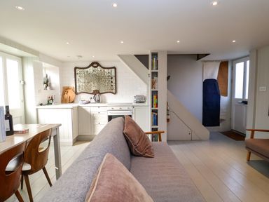 An open plan kitchen and living area with a grey sofa and wooden dining chairs at Mariners Cottage in Aldeburgh