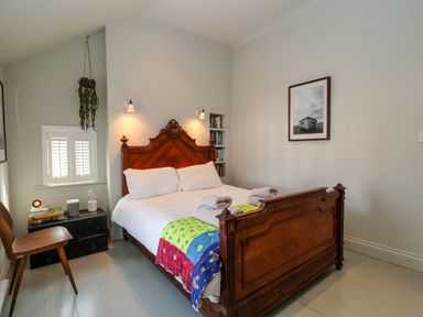 A bedroom with a wooden bed with white bedding and colorful cover in Mariners Cottage Aldeburgh