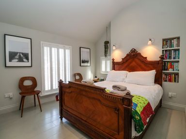 A bedroom with a wooden bed a colorful blanket two wooden chairs framed pictures and bookshelves at Mariners Cottage in Aldeburgh