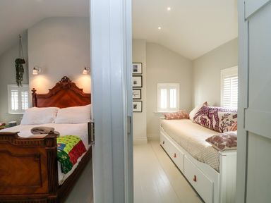 A bedroom with a wooden bed on the left and a room with a daybed and cushions on the right at Mariners Cottage in Aldeburgh