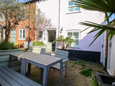 An outdoor patio with a table and chairs surrounded by plants and houses at Mariners Cottage in Aldeburgh