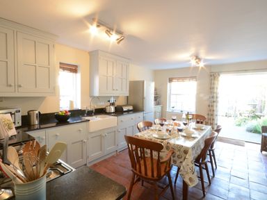A kitchen with white cabinets a dining table set for six and a door opening to a garden at Pebble Beach Cottage Aldeburgh