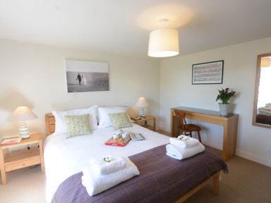 A bedroom with a double bed bedside tables lamps a wooden desk chair and a large mirror at Pebble Beach Cottage Aldeburgh