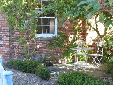 A small garden with a white metal table and two chairs next to a brick wall with a window at Pebble Beach Cottage Aldeburgh
