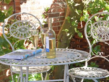A garden table with two glasses of white wine a bottle and a magazine with two chairs at Pebble Beach Cottage Aldeburgh