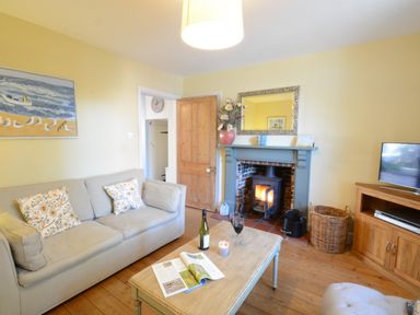A living room with a sofa a coffee table with a bottle and glasses a fireplace and a television at Pebble Beach Cottage Aldeburgh