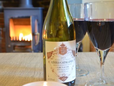 A bottle of red wine and two glasses of wine on a table with a fireplace in the background at Pebble Beach Cottage Aldeburgh
