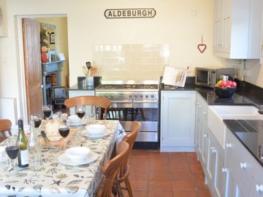 A kitchen with a dining table set with wine glasses and bowls and a stove with cabinets at Pebble Beach Cottage Aldeburgh