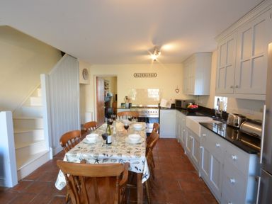 A kitchen with a dining table set for six next to white cabinets and a staircase at Pebble Beach Cottage Aldeburgh